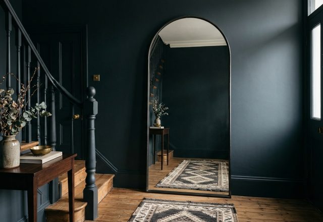 A stunning narrow foyer featuring deep blue-black Farrow and Ball Railings walls and a large arched mirror to illustrate narrow entryway ideas.