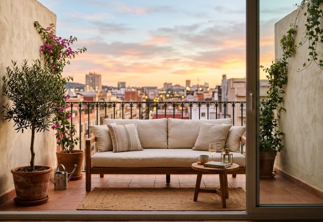 A hero focal visual of a modern small apartment balcony featuring a low-profile teak sofa, limewash walls in Benjamin Moore Swiss Coffee, and sunset lighting.