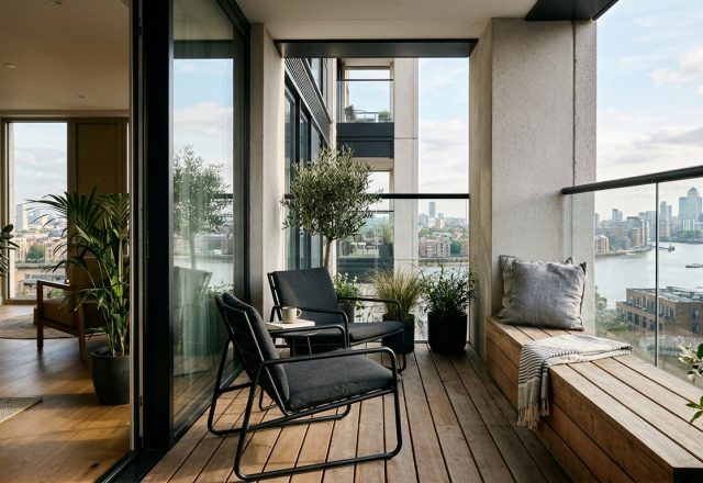 A sophisticated urban balcony featuring slimline black metal chairs and a built-in wooden bench, demonstrating primary circulation clearances for small apartment balcony ideas.