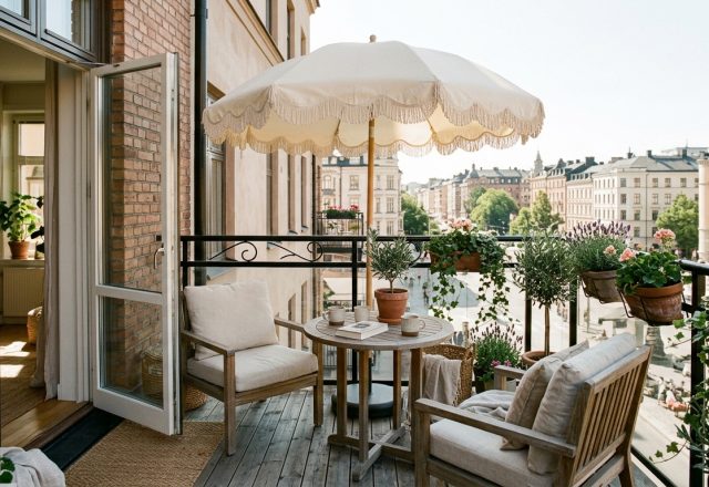 A sun-drenched urban balcony featuring a Joanna Gaines patio umbrella with scalloped edges, defining a sophisticated outdoor lounging zone with linen textures.