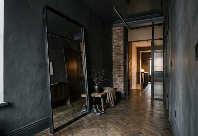 A moody Manhattan entryway with dark charcoal walls and a large leaning floor mirror reflecting natural light to enhance spatial depth, following bjorn wallander manhattan apartment tour decor ideas.