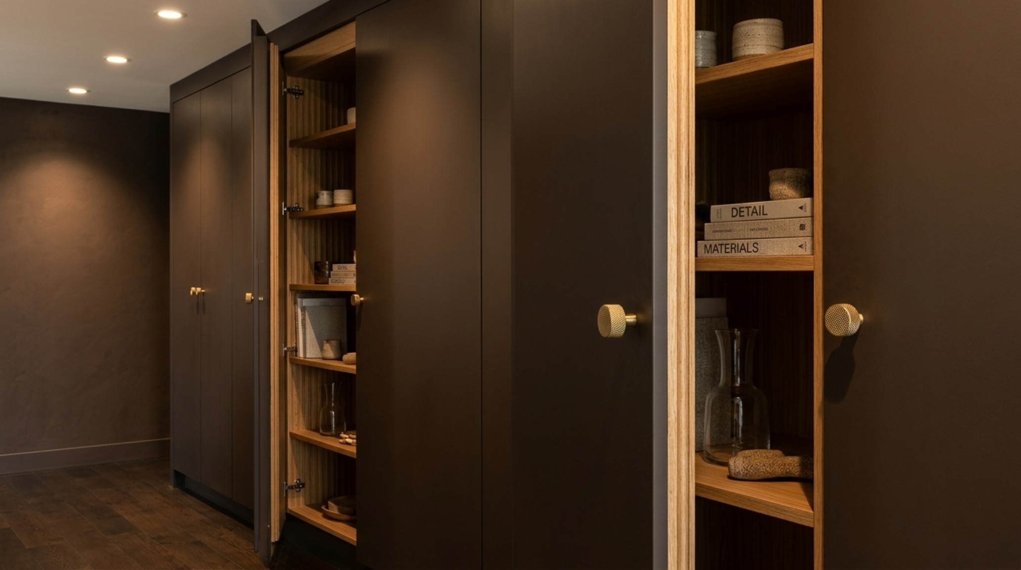 Detailed view of custom hidden storage cabinetry painted in a matte brown shade, showcasing fluted oak interiors and knurled brass hardware.
