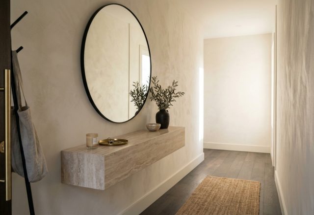 Modern narrow entryway ideas layout featuring a minimalist floating marble console and a tall circular mirror against limewash walls.