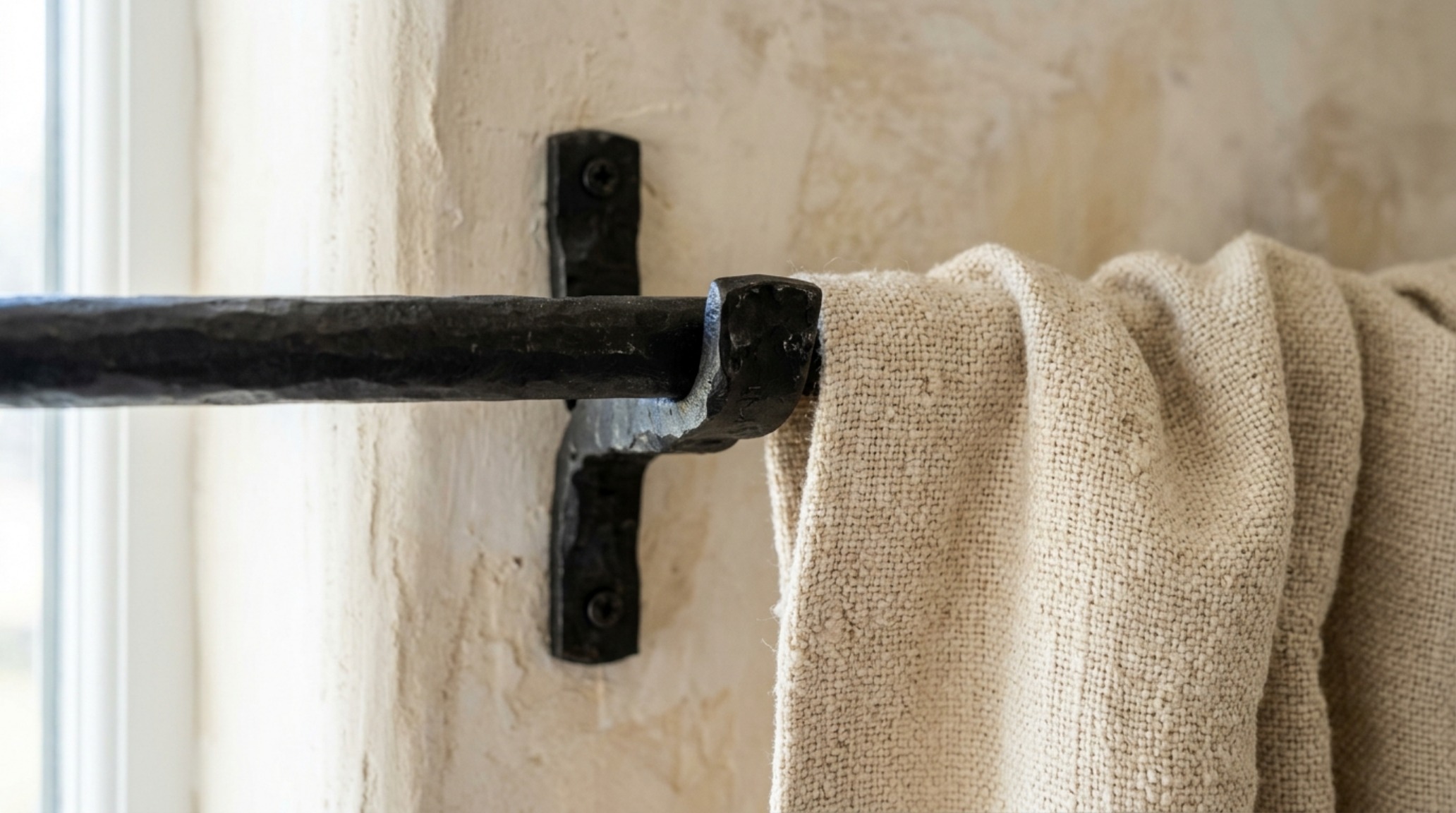 Close-up of unlacquered brass curtain rings on a matte black rod against a limewash wall with farmhouse fresh how window treatments set decor ideas.
