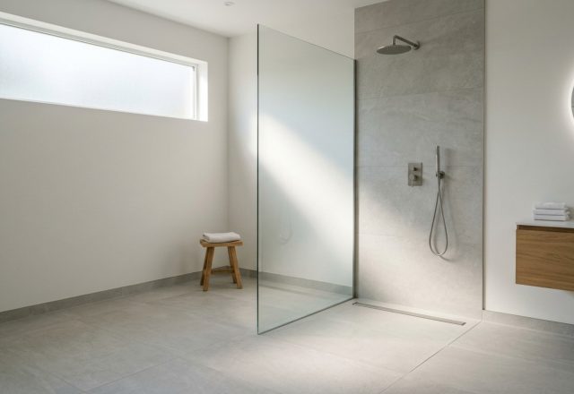 curbless wet room design featuring a seamless transition from light gray porcelain floor tiles to a minimalist glass-enclosed shower with a concealed linear drain