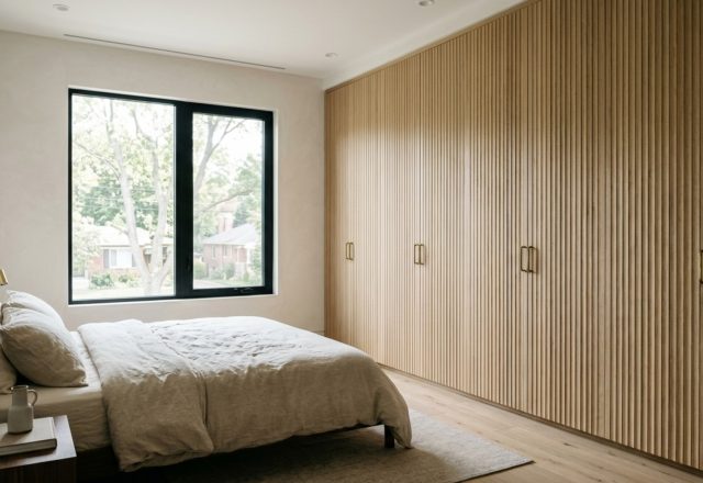 A bright urban bedroom featuring floor-to-ceiling closet doors decor ideas with fluted white oak panels and soft 2700K ambient lighting reflecting off limewash walls.