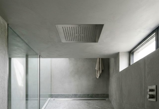flush ceiling shower head installation seamlessly integrated into a soft-grey Tadelakt plaster ceiling with perimeter LED cove lighting.