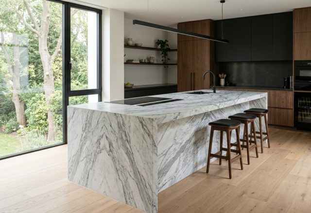 waterfall edge island ideas featuring a bookmatched Arabescato marble slab with precision mitered corners and a recessed brass toe-kick.
