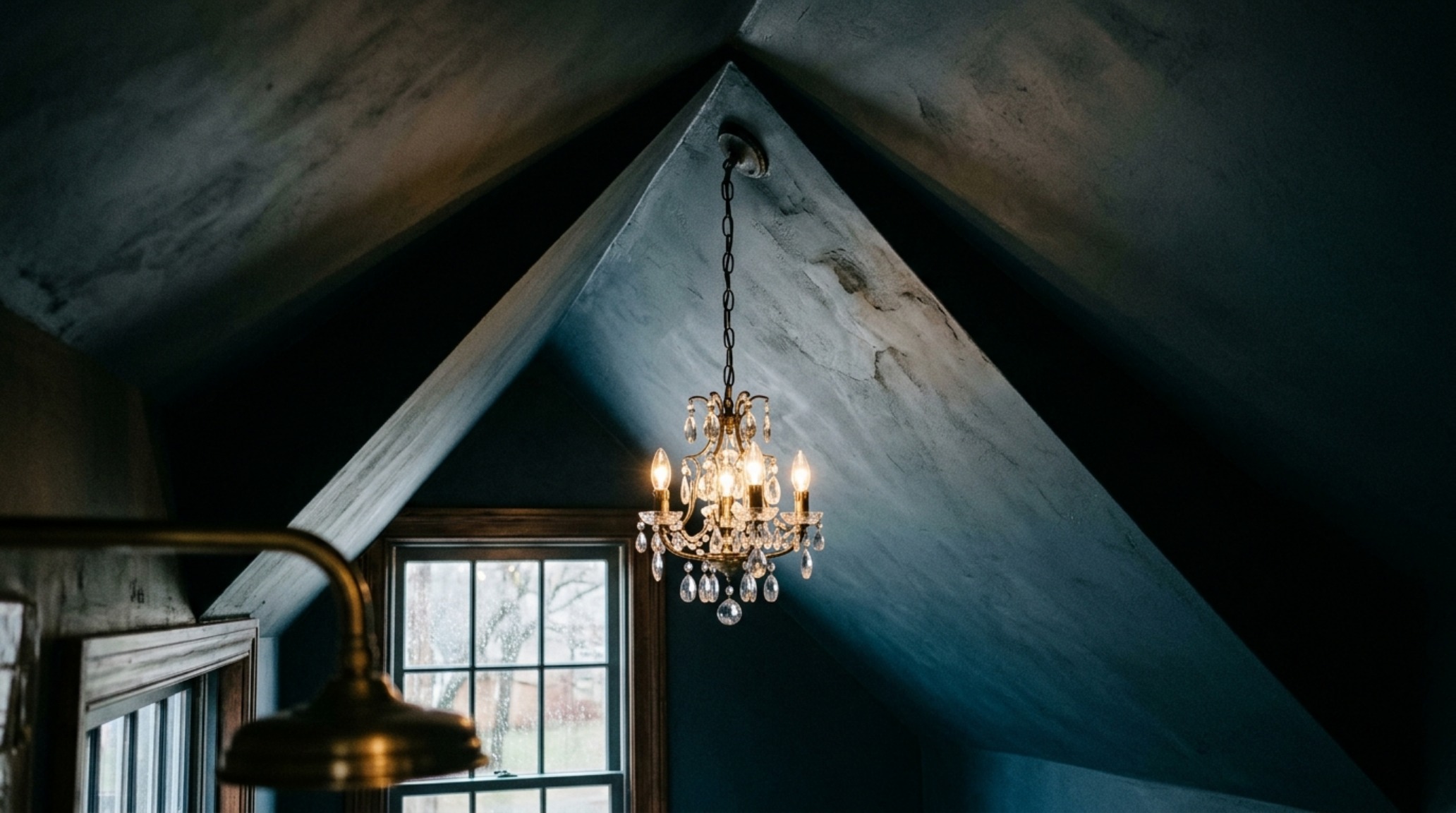 Interior view of a powder room under stairs looking toward the ceiling, showcasing how the sloping geometry is highlighted by a designer chandelier.