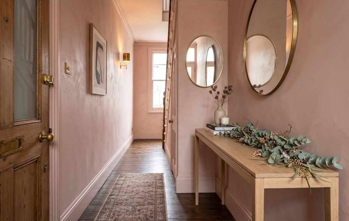 A narrow entryway featuring Farrow and Ball Setting Plaster walls, a slim white oak console table, and a minimalist eucalyptus garland under warm 2700K lighting.