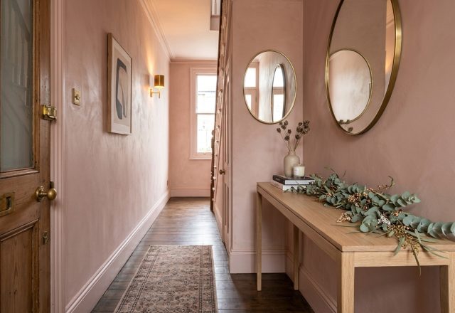 A narrow entryway featuring Farrow and Ball Setting Plaster walls, a slim white oak console table, and a minimalist eucalyptus garland under warm 2700K lighting.