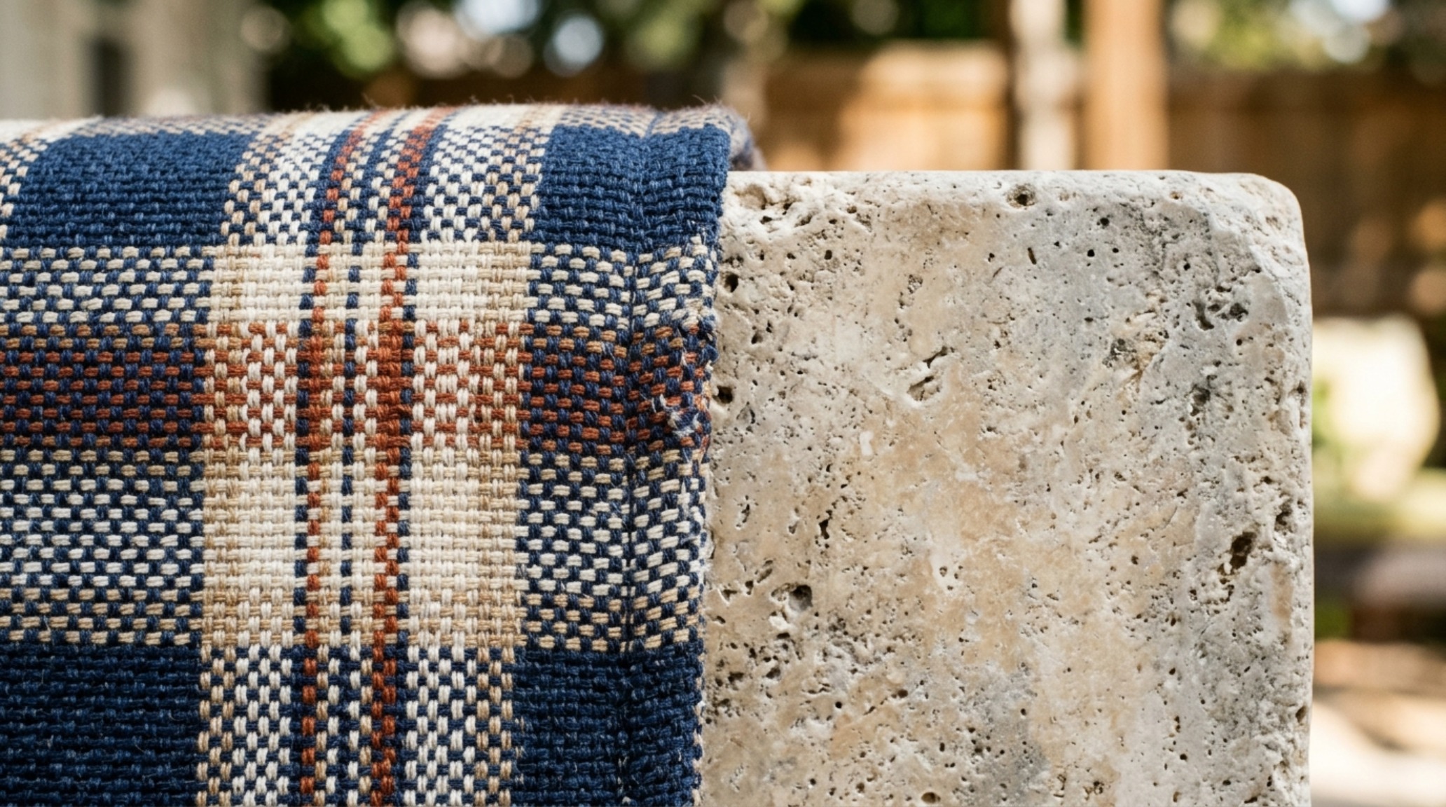 Close-up of Sunbrella plaid fabric textures layered with a smooth honed travertine stone coffee table on a city balcony.