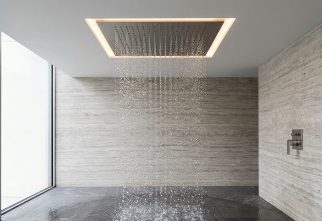 Dornbracht Rain Sky M installation integrated into a seamless dropped ceiling with warm 2700K LED accent lighting and silver travertine walls.