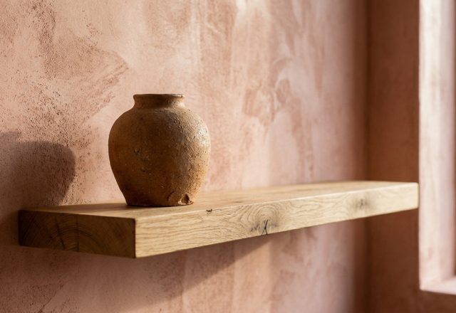 Tactile interior textures showcasing a hand-applied limewash wall in Farrow & Ball Setting Plaster with a raw ceramic vessel on a floating oak shelf.