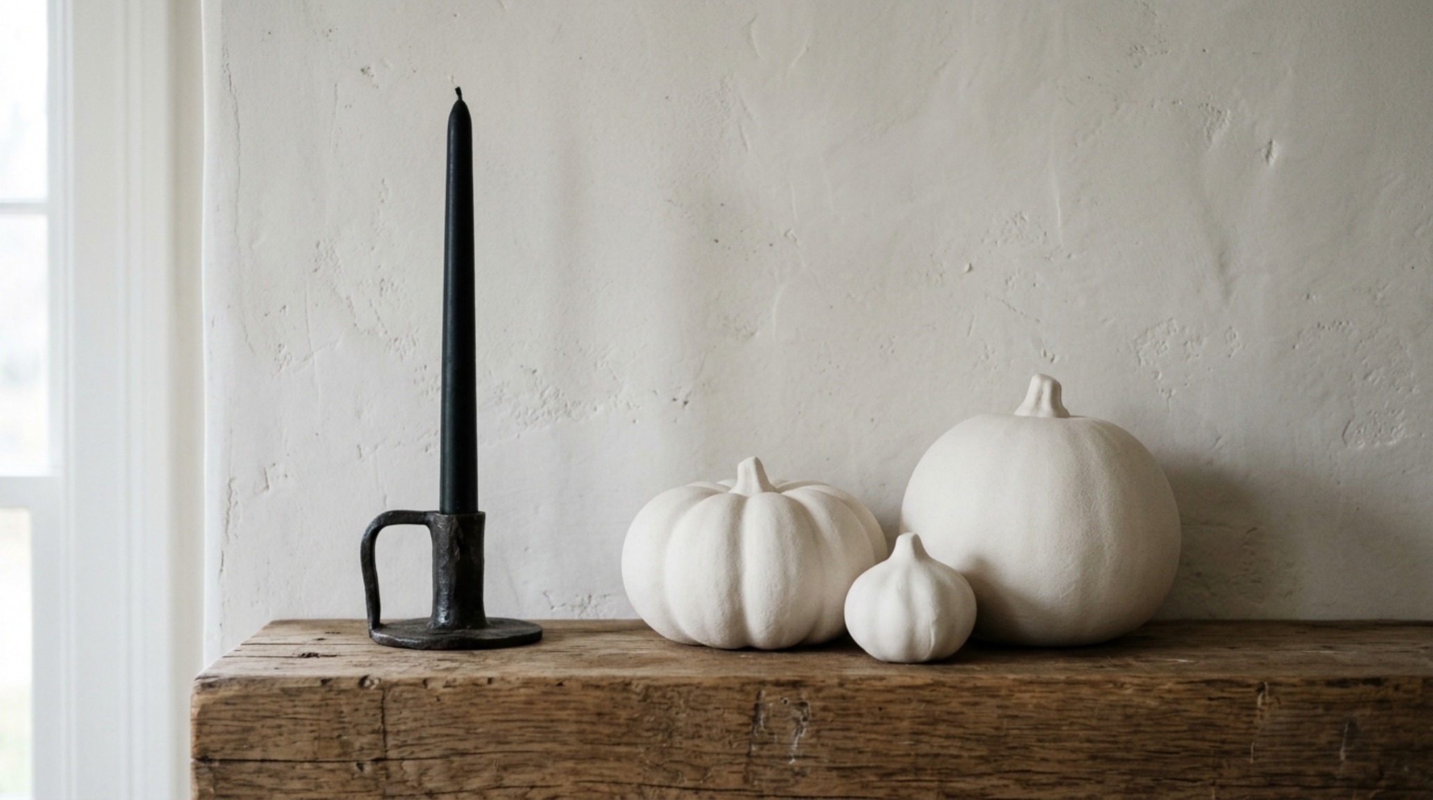 minimalist halloween mantel decor with asymmetrical placement of three matte white ceramic gourds and a solitary beeswax candle