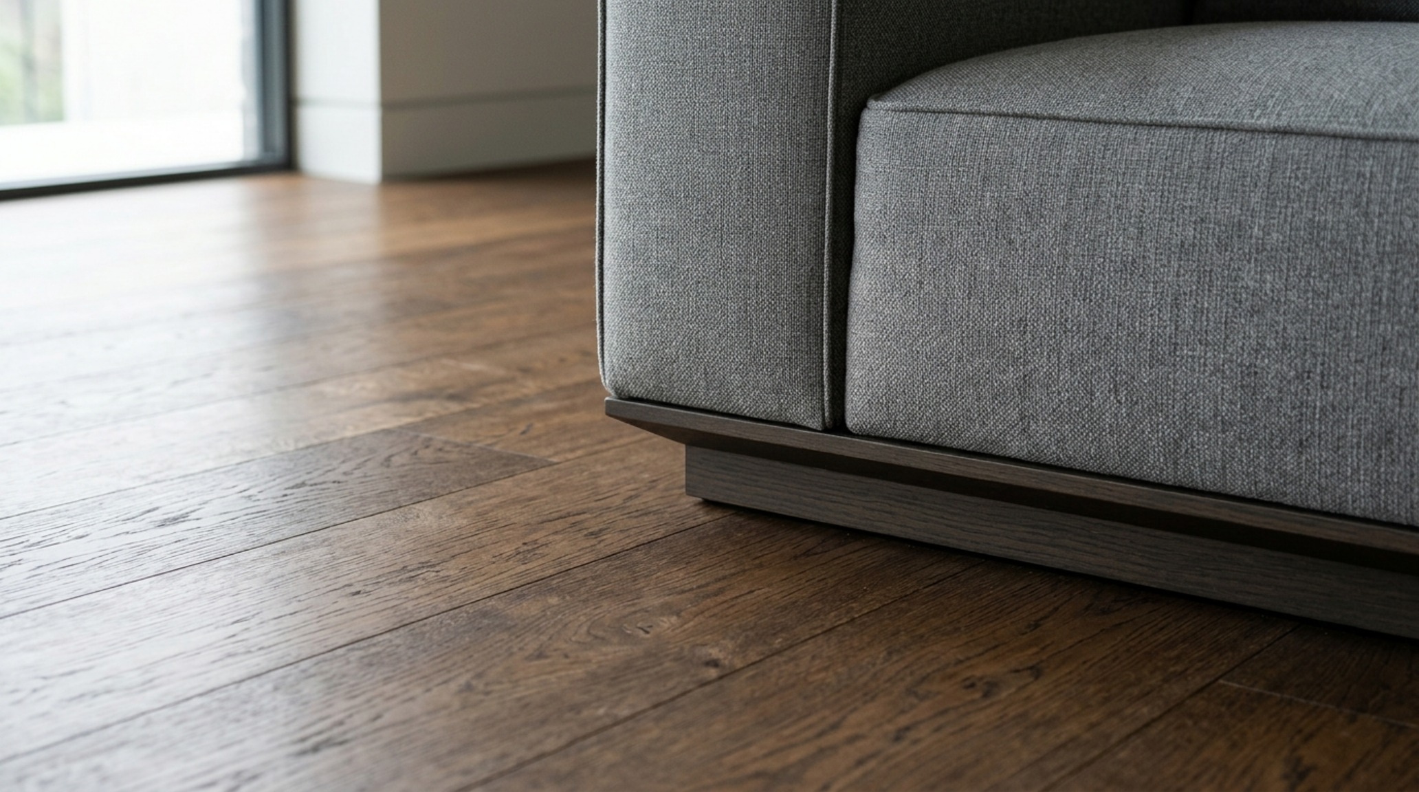 Architectural detail of a recessed plinth base on a modular sofa, creating a floating effect over wide-plank oak floors.