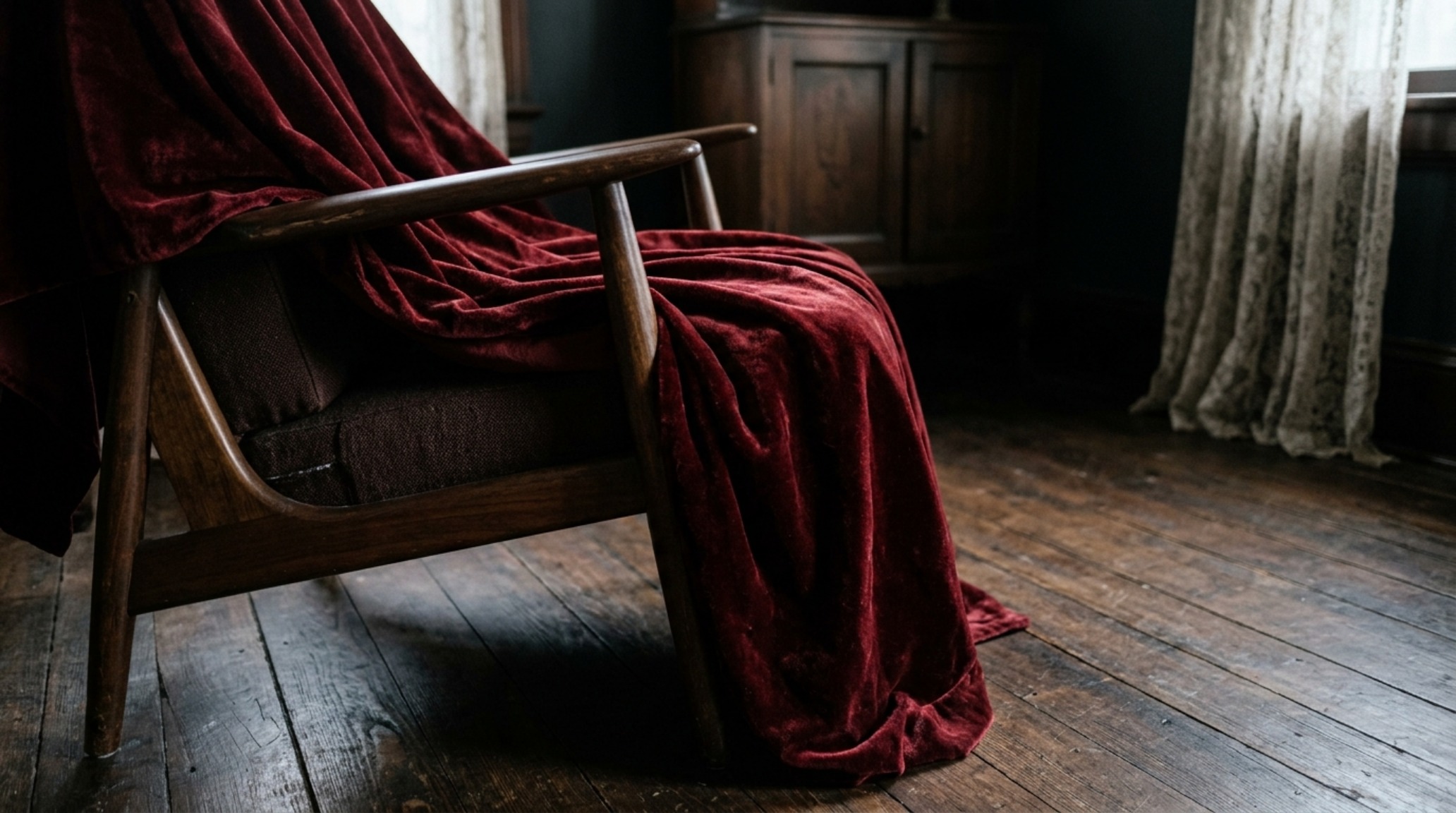 Victorian gothic materiality displayed through a crushed velvet oxblood throw draped over a blackened steel ottoman in a moody library.