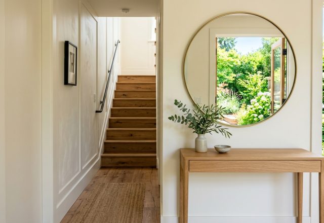 A bright summer entryway featuring a minimalist white oak console, large round mirror, and 36-inch clear circulation path, demonstrating narrow entryway ideas architecture.