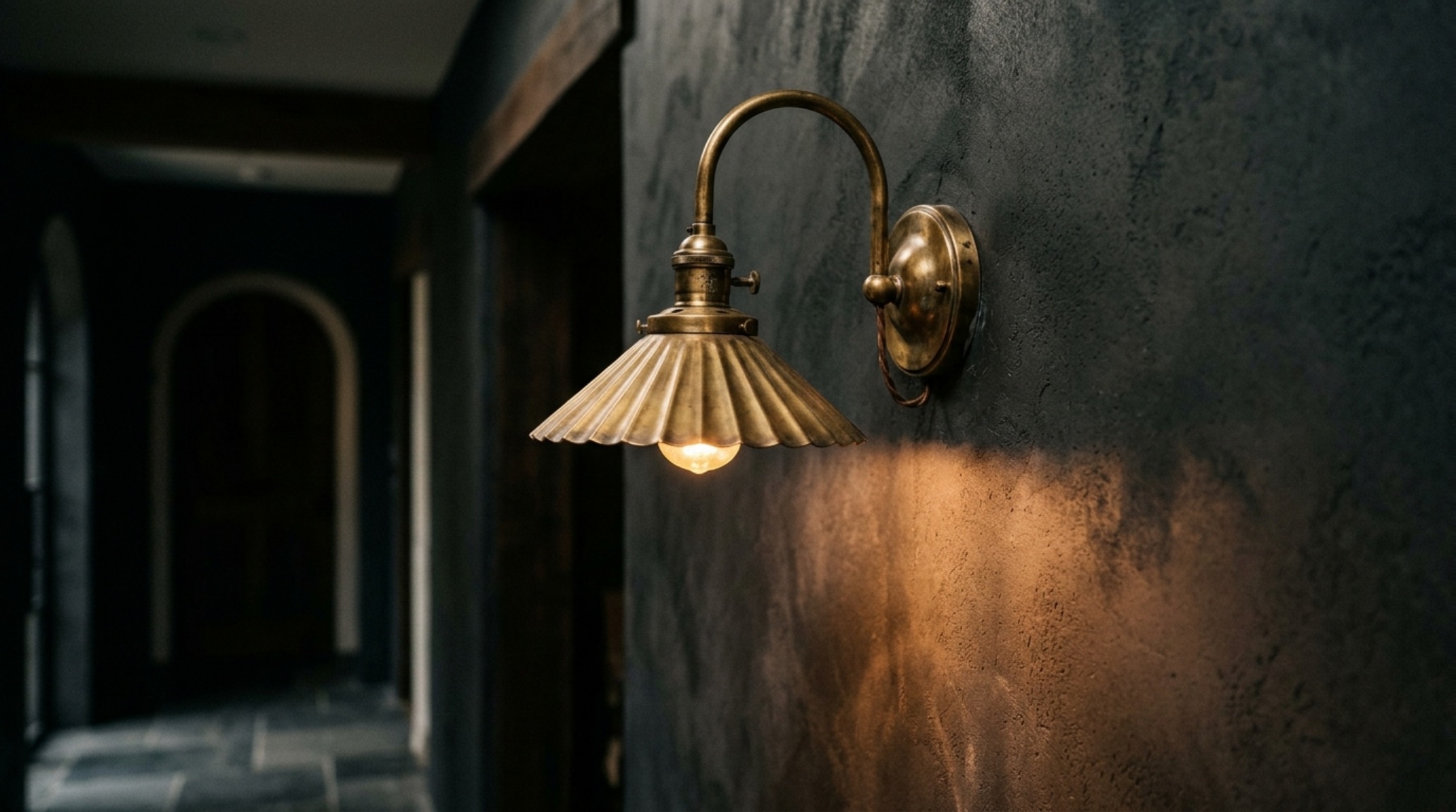 Atmospheric hallway lighting showing a designer brass sconce casting a soft 2700K amber glow against a textured limewash wall in a compact foyer.