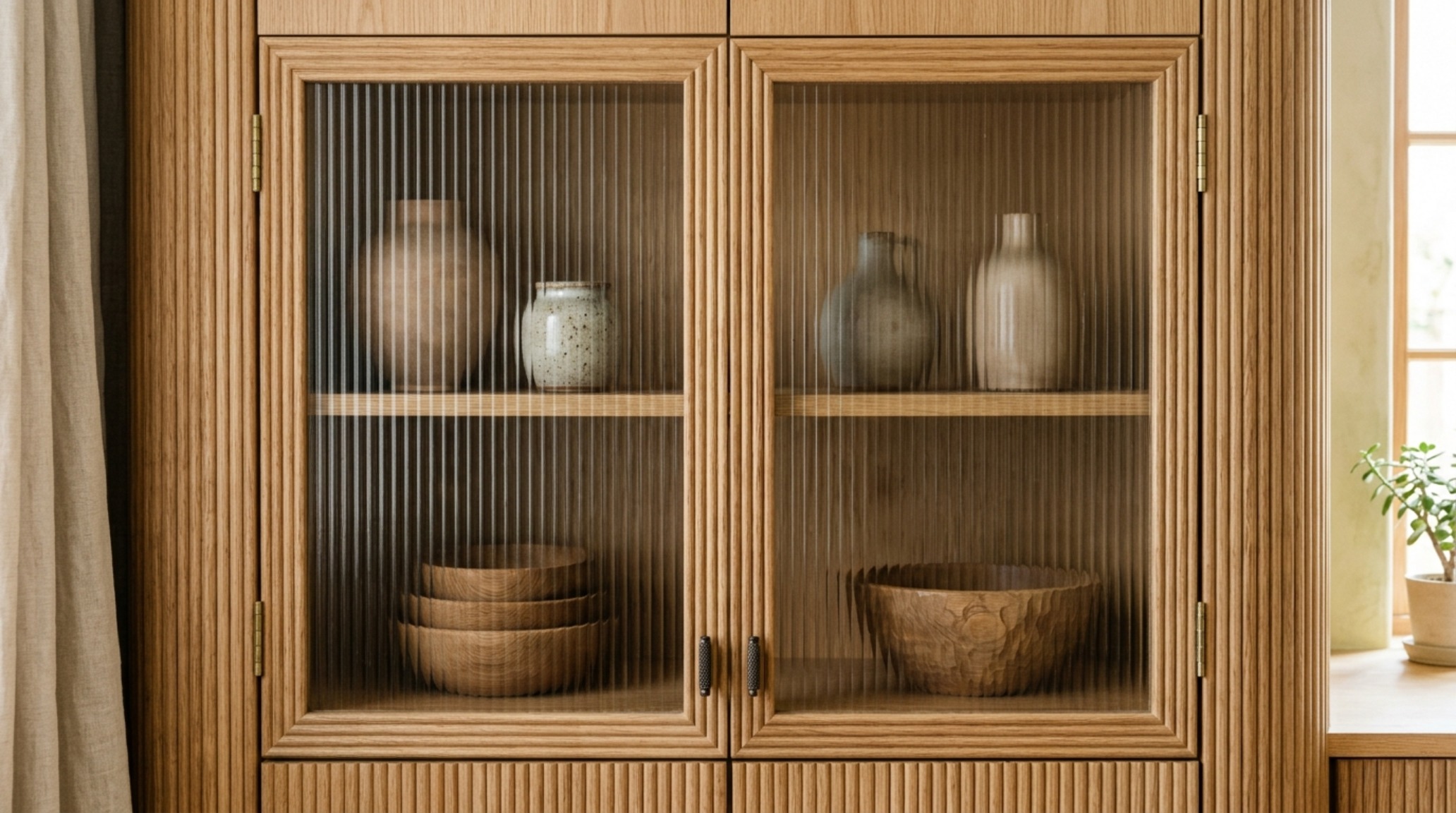 Reeded glass-front upper cabinet installation displaying a curated collection of artisanal stoneware and ceramics in a modern kitchen. Reeded glass-front upper cabinet installation displaying a curated collection of artisanal stoneware and ceramics in a modern kitchen.