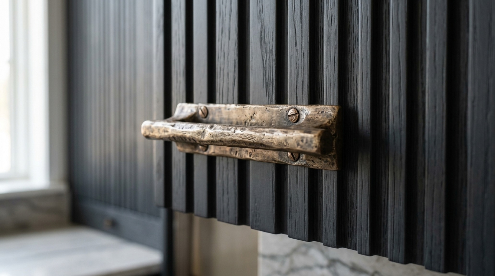 Bespoke cabinet hardware styling featuring hand-finished bronze pulls on a dark charcoal cabinet door under natural morning sunlight. Bespoke cabinet hardware styling featuring hand-finished bronze pulls on a dark charcoal cabinet door under natural morning sunlight.