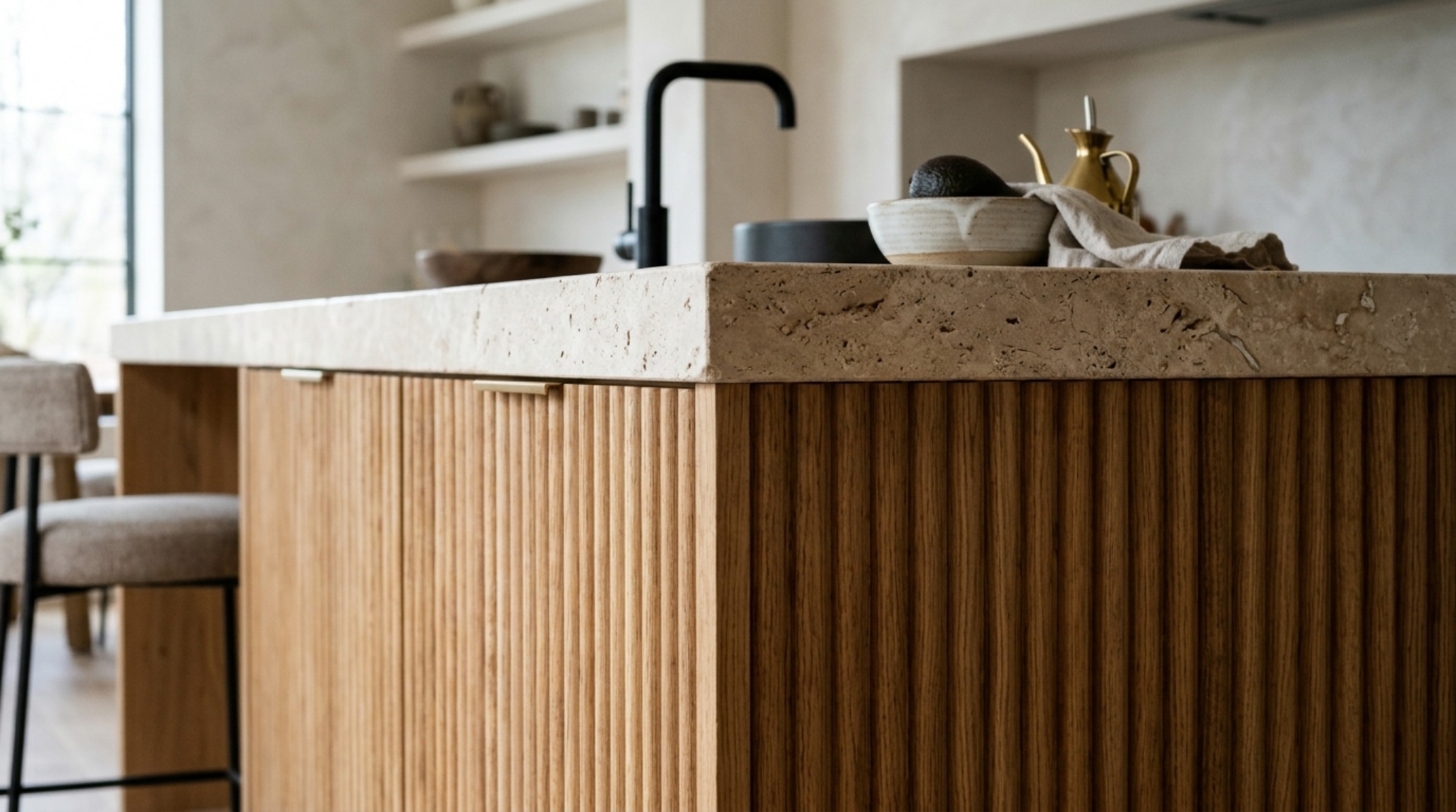 sustainable material selection showcased through a kitchen island of fluted white oak paired with a matte honed travertine countertop and integrated brass fixtures. sustainable material selection showcased through a kitchen island of fluted white oak paired with a matte honed travertine countertop and integrated brass fixtures.