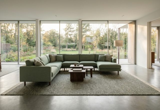 A floating sage green sectional sofa in a large open-plan living room with floor-to-ceiling windows and 36-inch circulation paths.