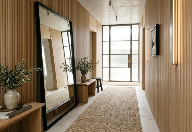 A grand narrow entryway featuring a 7-foot tall minimalist mirror, a long jute runner rug, and white oak walls reflecting natural light.
