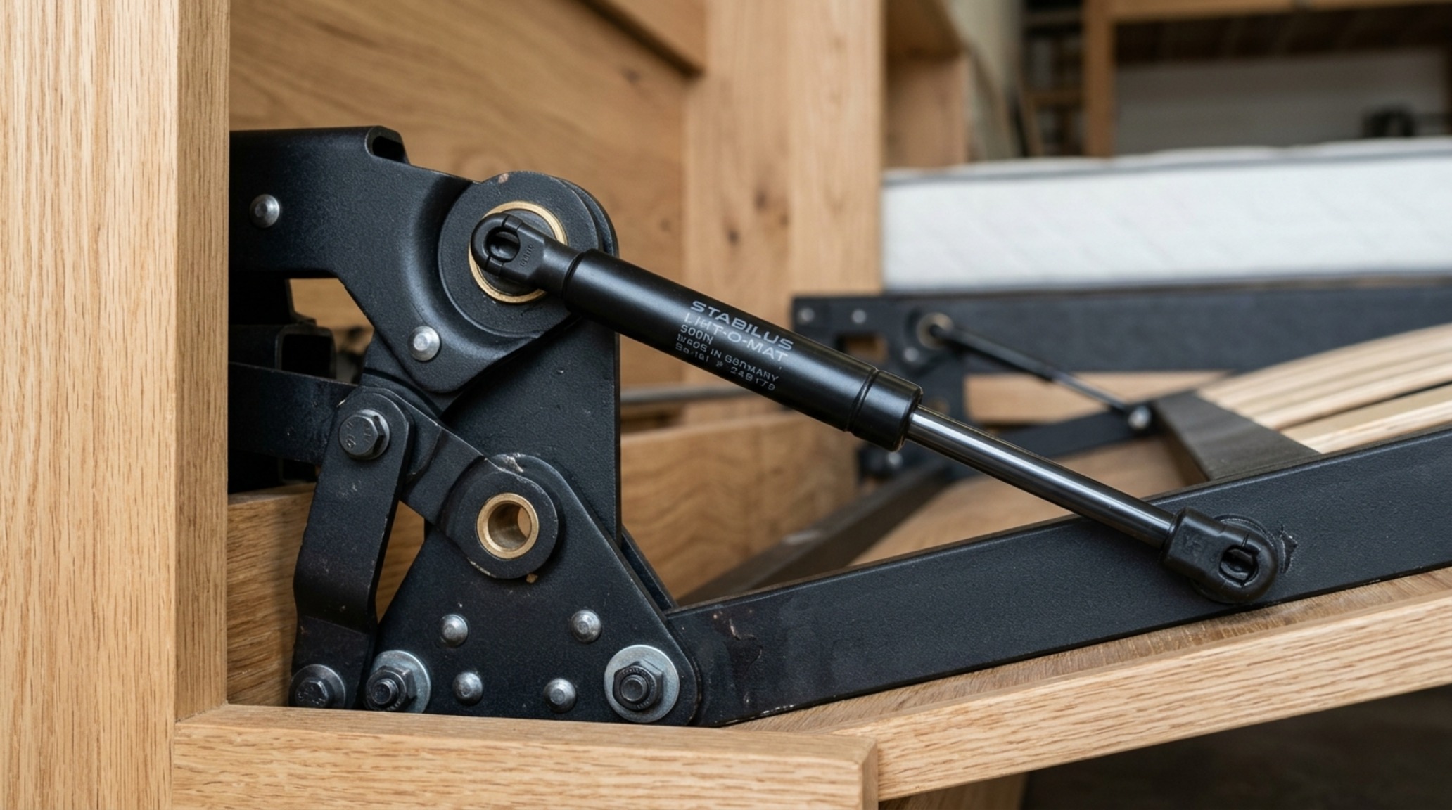 Gas-piston fold down bed mechanism close-up showing the sleek brushed steel hardware and smooth hydraulic arm in a high-end millwork system. Gas-piston fold down bed mechanism close-up showing the sleek brushed steel hardware and smooth hydraulic arm in a high-end millwork system.
