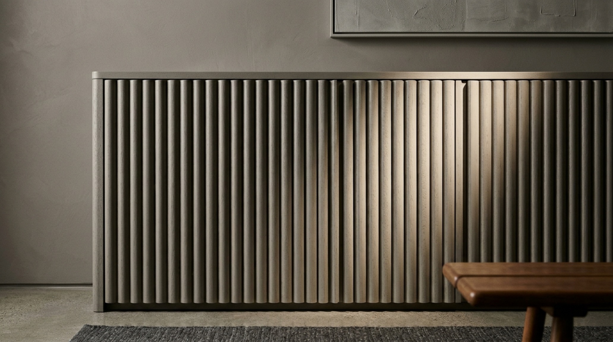 Architectural detail of a fluted cabinet door finished in a warm taupe, with directional lighting casting soft shadows that define the furniture's structural form.