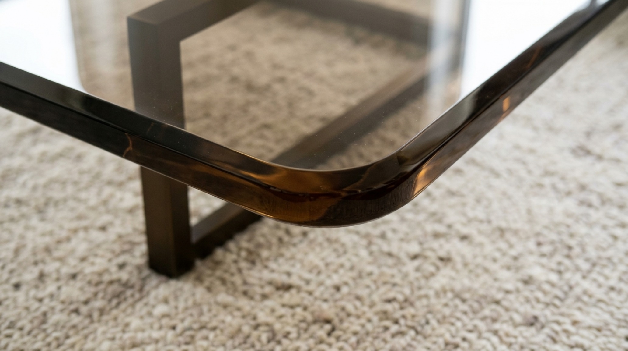 Close-up of high-quality tempered glass showing the slight green jewel-tint edge against a neutral designer rug. Close-up of high-quality tempered glass showing the slight green jewel-tint edge against a neutral designer rug.