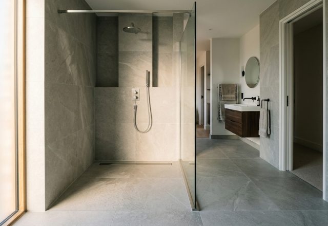 Wet room design trends featuring a curbless shower entry with a linear drain and floor-to-ceiling structural glass panel for an open-concept aesthetic.