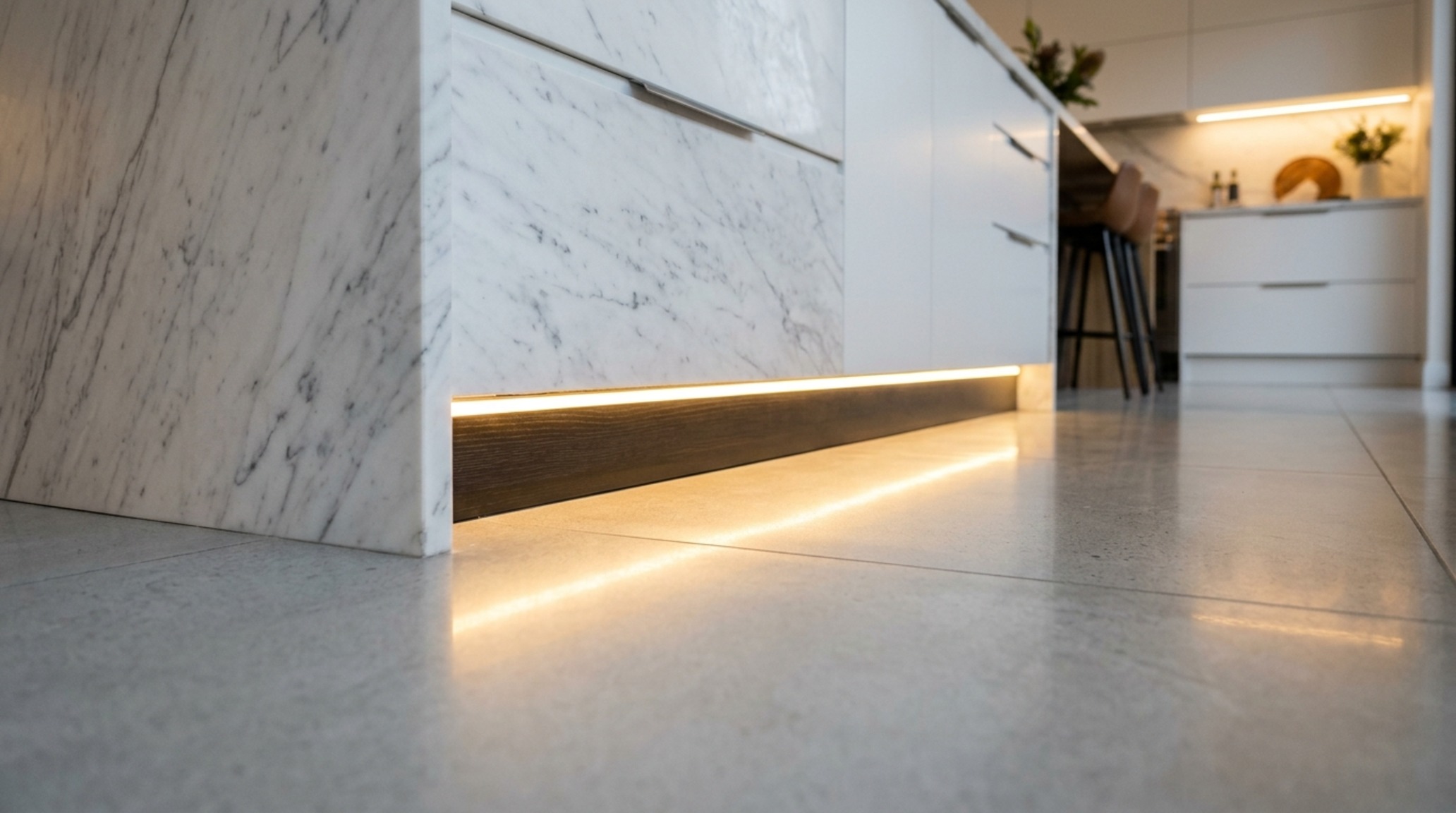 DIY architectural lighting installed under kitchen island toe-kicks to create a weightless floating effect on polished concrete floors.