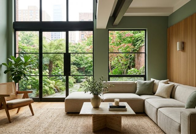 A bright, airy living room featuring sage green living room ideas with a low-profile beige sectional and floor-to-ceiling windows.