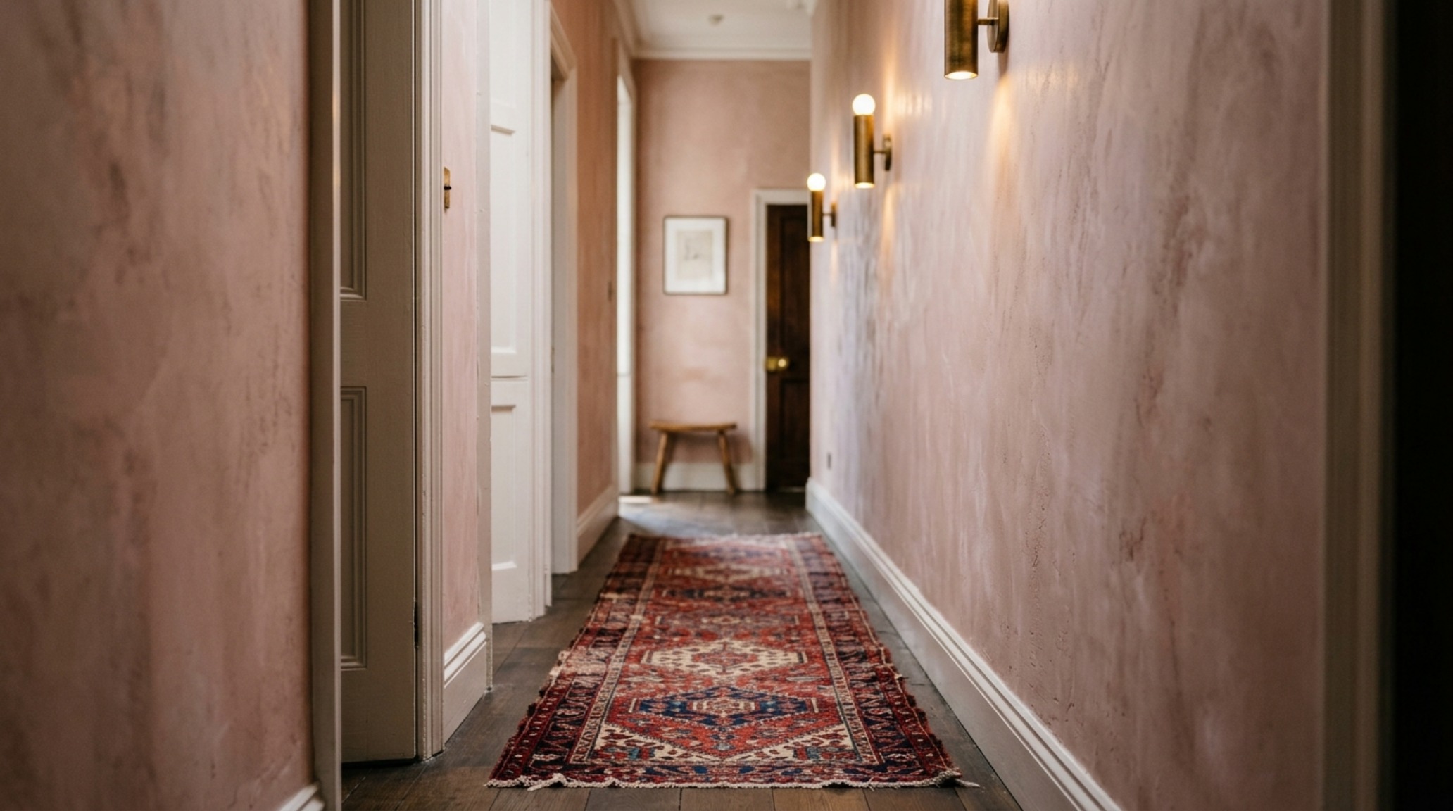 Editorial shot of a narrow entryway with limewash walls, a vintage jute runner, and directional architectural lighting. Editorial shot of a narrow entryway with limewash walls, a vintage jute runner, and directional architectural lighting.