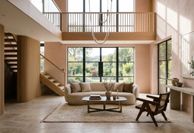 sustainable luxury home materials like honed travertine and fluted white oak in a double-height living space with massive floor-to-ceiling windows.