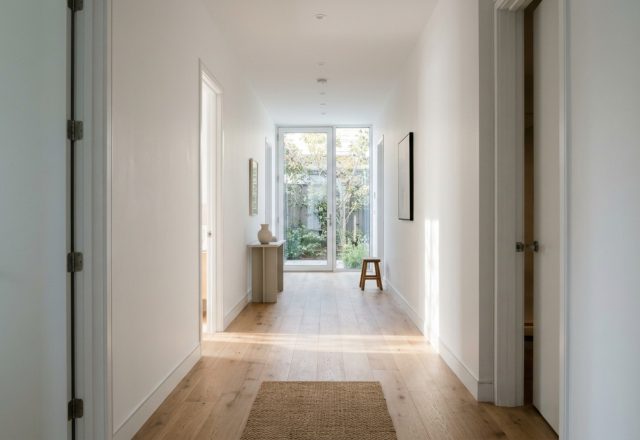 Residential spatial flow illustrated through a wide-angle view of a minimalist hallway with 36-inch clearances and natural oak flooring.
