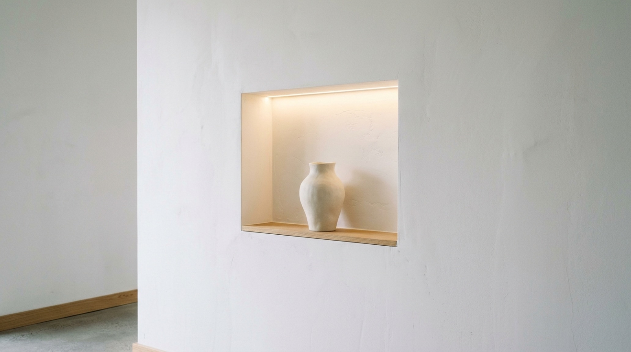 A custom-built recessed niche in a white wall displaying a single piece of organic ceramic art, illustrating minimalist white house decor ideas.