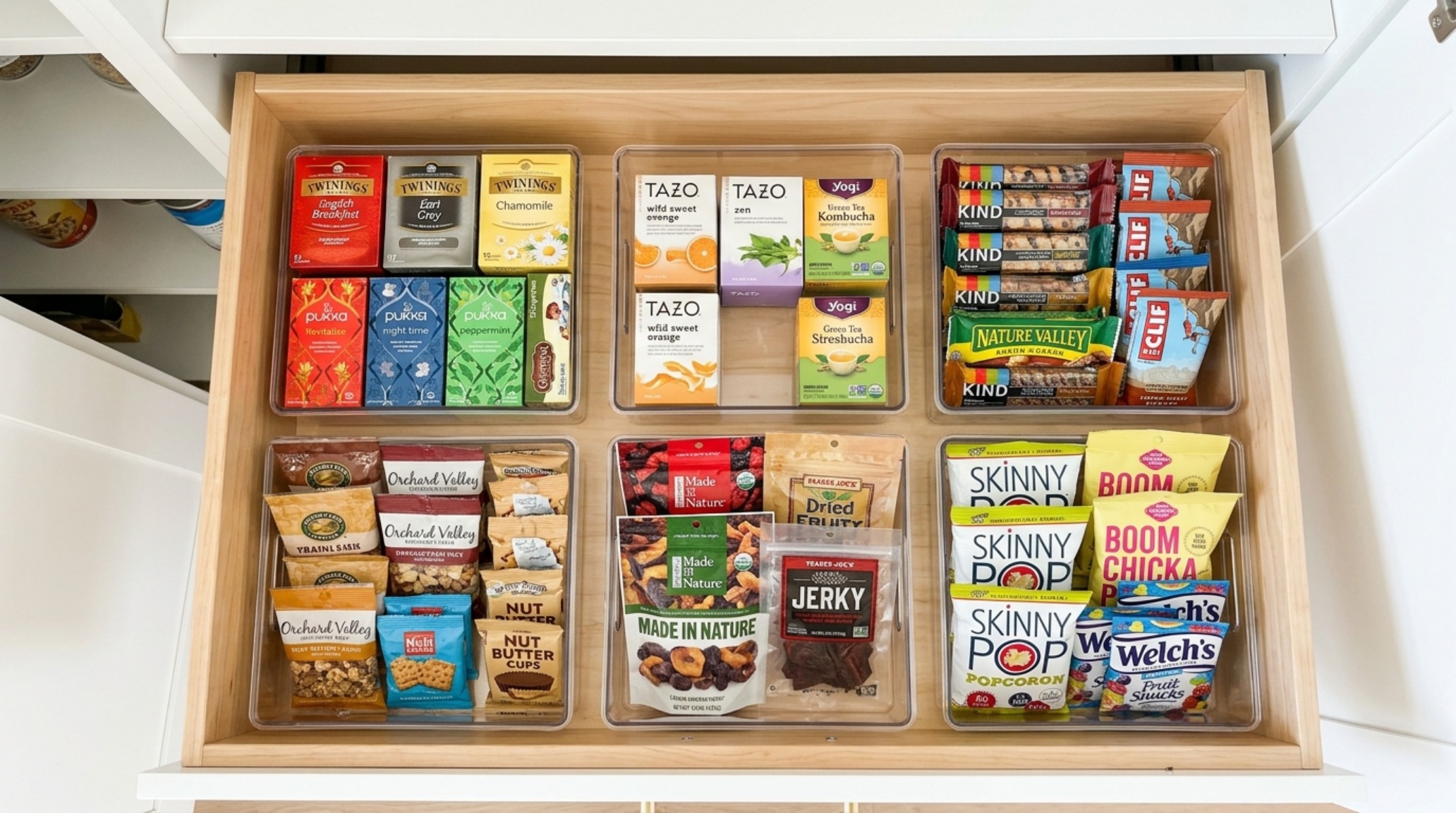 Top-down view of a pantry drawer featuring clear acrylic pantry storage bins used to segment tea and snack bars.