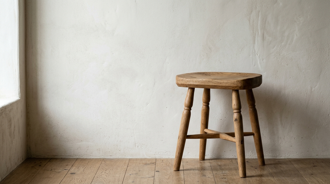Close-up of textured lime wash walls and a single wooden stool in a minimalist hallway.