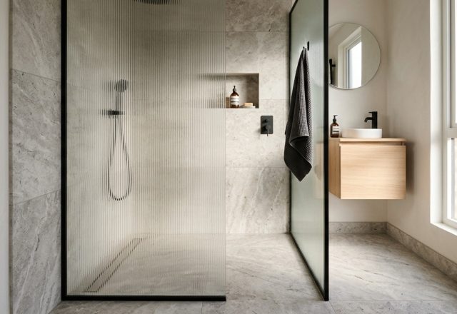 Wet room conversions for tiny spaces featuring a seamless limestone floor, hidden linear drain, and a single fixed fluted glass panel for a curbless transition.