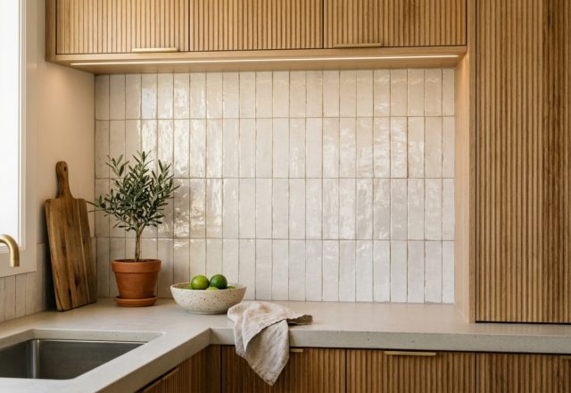 A kitchen backsplash featuring vertically stacked glossy Zellige tiles in a soft bone white, paired with fluted white oak cabinetry and warm 2700K under-cabinet lighting.