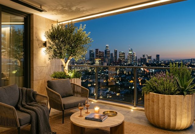 A luxury high-rise balcony at dusk featuring 2700K warm ambient lighting, fluted stone planters with olive trees, and sophisticated small apartment balcony ideas for modern urban living.