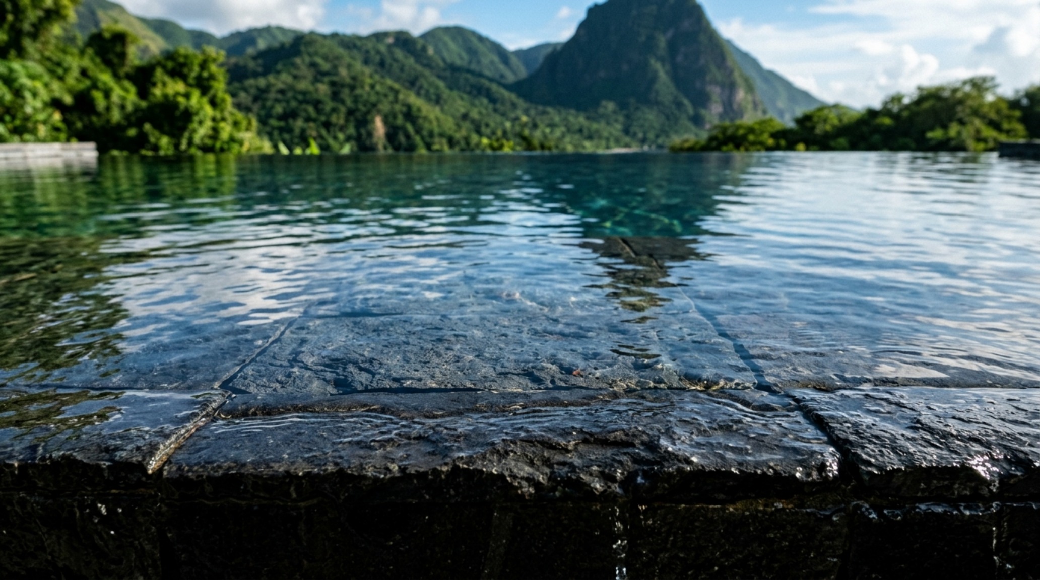 volcanic stone pool tiling in a matte basalt finish creating a mirror-like surface that reflects the tropical sunset and natural rock walls volcanic stone pool tiling in a matte basalt finish creating a mirror-like surface that reflects the tropical sunset and natural rock walls