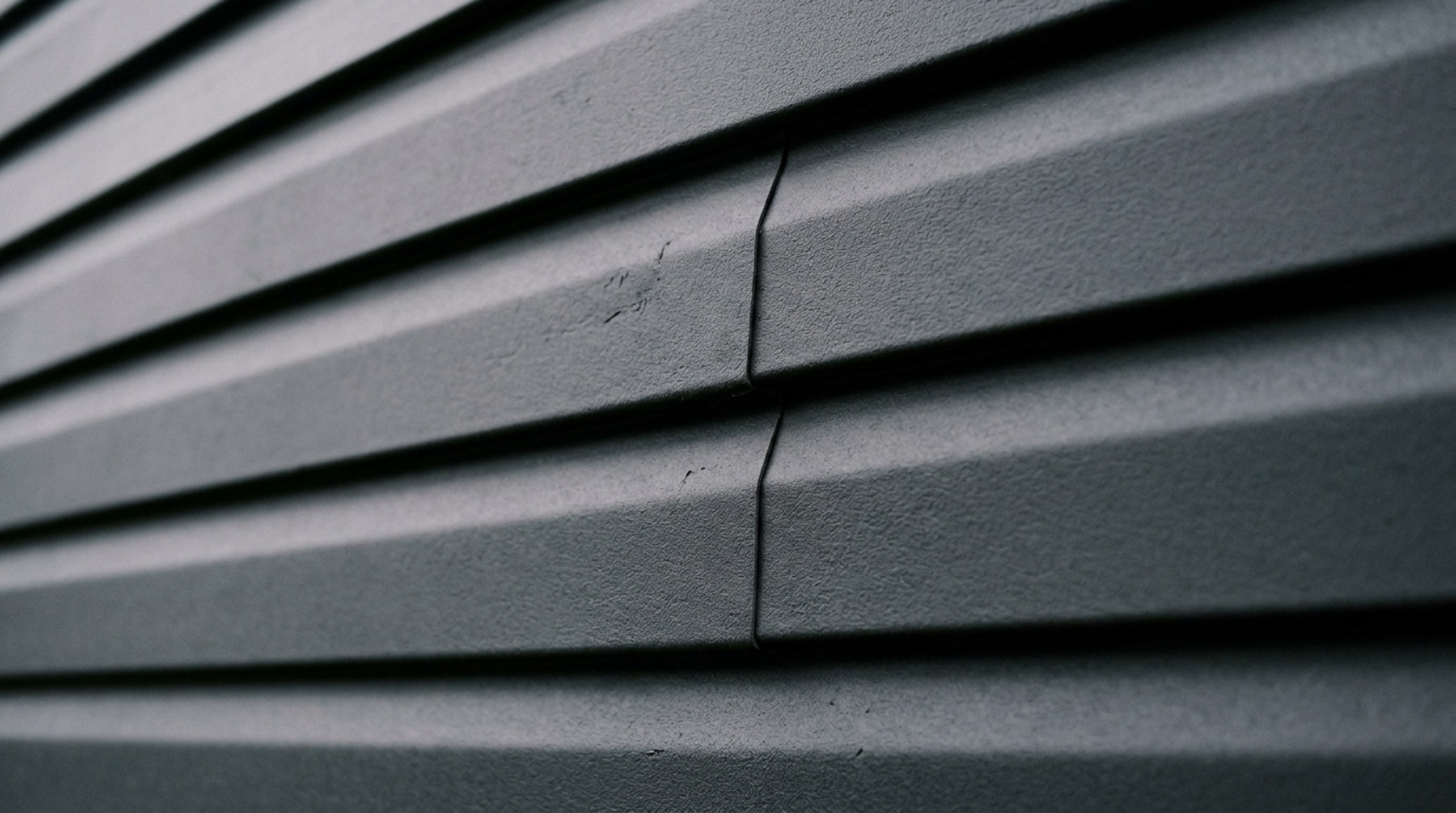 A macro detail of vinyl siding painted in a flat, desaturated charcoal, demonstrating how a matte finish eliminates plastic glare and creates sophisticated shadow play. A macro detail of vinyl siding painted in a flat, desaturated charcoal, demonstrating how a matte finish eliminates plastic glare and creates sophisticated shadow play.