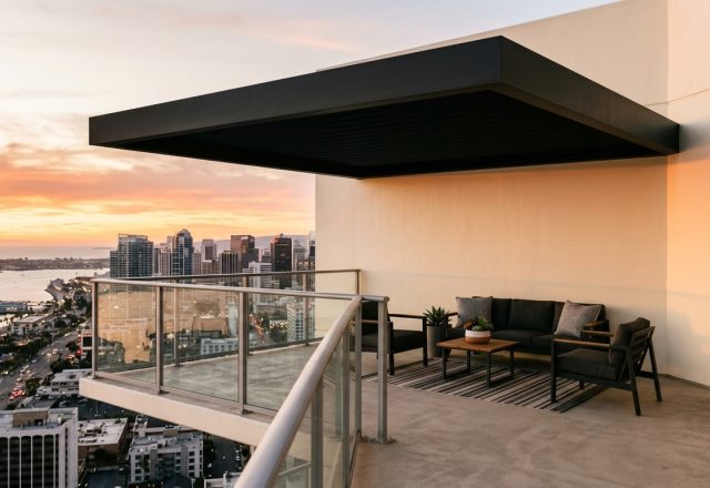 A sleek cantilevered patio cover structure expands the volume of a modern urban terrace, showcasing innovative small apartment balcony ideas with panoramic city views.