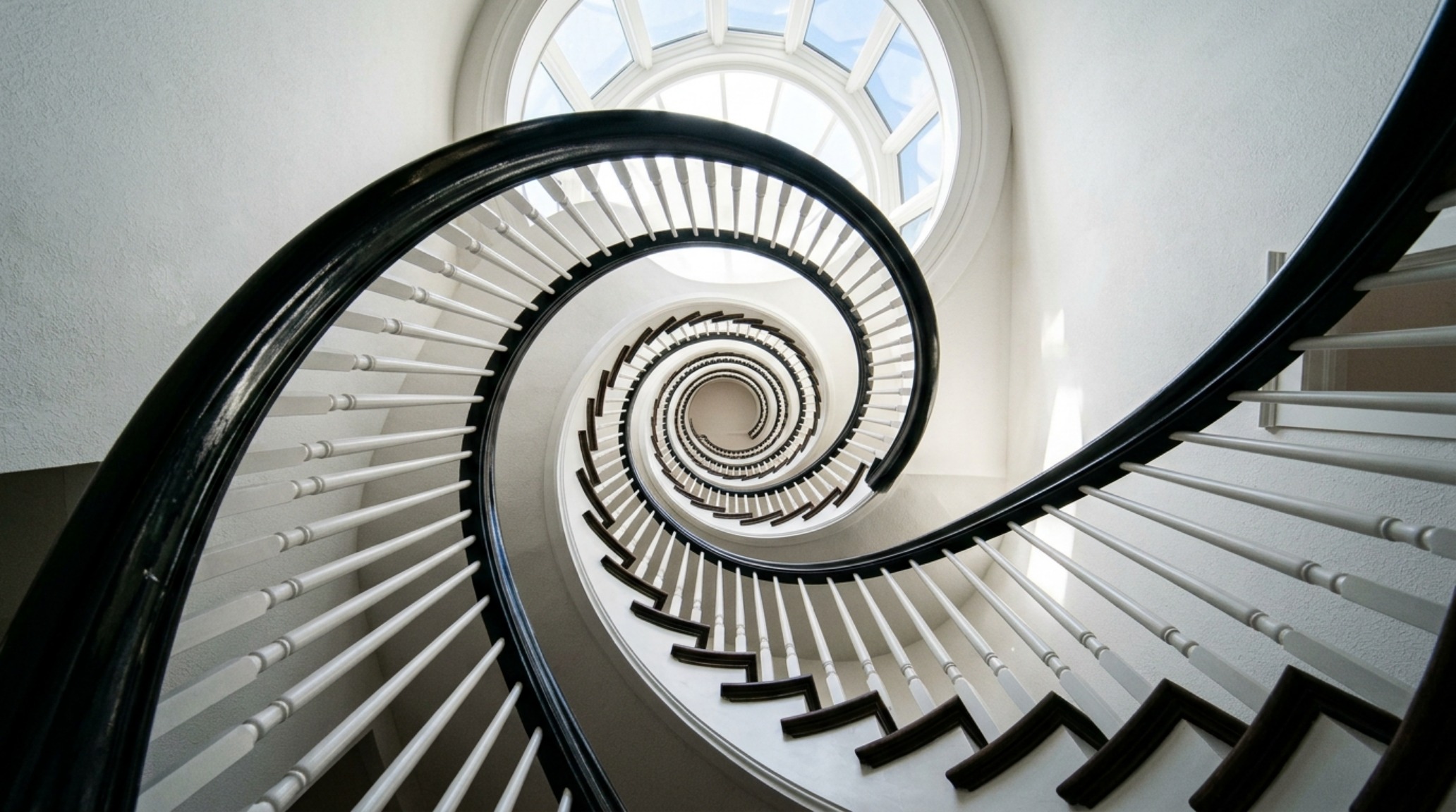 A grand entrance featuring a semi-gloss grand staircase railing in a dark walnut stain, showing the level of detail and light reflection on curved wood surfaces. A grand entrance featuring a semi-gloss grand staircase railing in a dark walnut stain, showing the level of detail and light reflection on curved wood surfaces.