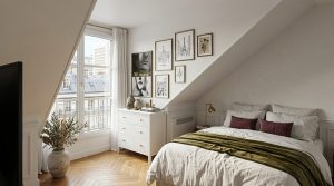 Cozy attic bedroom decor featuring slanted walls, a white dresser, and herringbone wood flooring overlooking a french balcony.