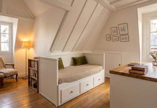 Bright attic bedroom design featuring sloped ceilings, a white built-in daybed, and a wooden desk near a window.