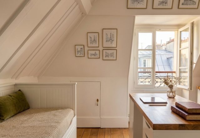 Cozy attic bedroom office combo featuring a built-in daybed, slanted white beams, and a wooden desk near a bright window.
